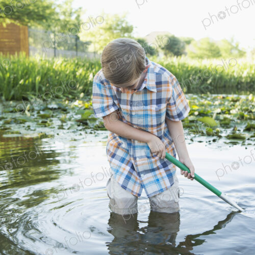 A young boy standing thigh deep in water, using a net to scoop up interesting objects… A young boy standing thigh deep in water, using a net to scoop up interesting objects…