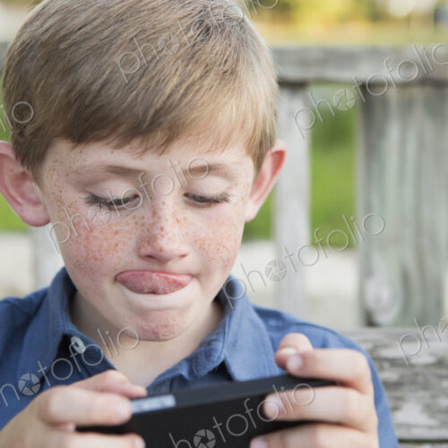 A young boy using a hand held electronic tablet or game and concentrating, sticking…