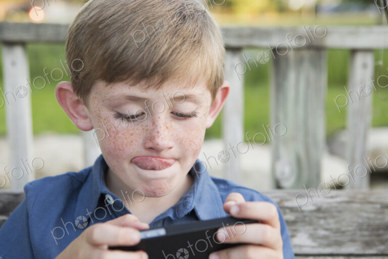 A young boy using a hand held electronic tablet or game and concentrating, sticking…