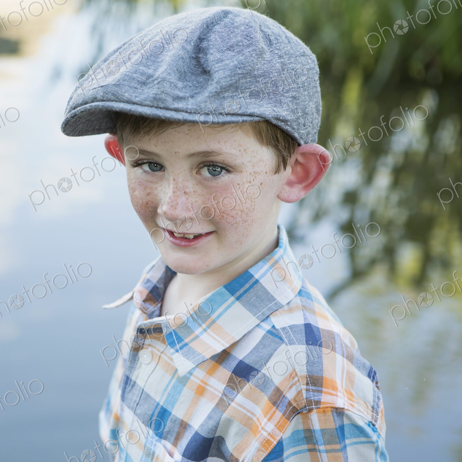 A young boy wearing a checked shirt and cloth cap with a large brim standing on a…