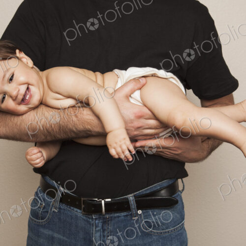 A young boy wearing cloth diapers being held by his father in his arms. A young boy wearing cloth diapers being held by his father in his arms.