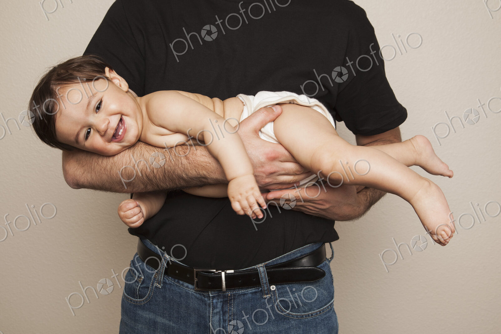 A young boy wearing cloth diapers being held by his father in his arms.