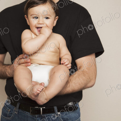 A young boy wearing cloth diapers being held by his father in his arms. A young boy wearing cloth diapers being held by his father in his arms.