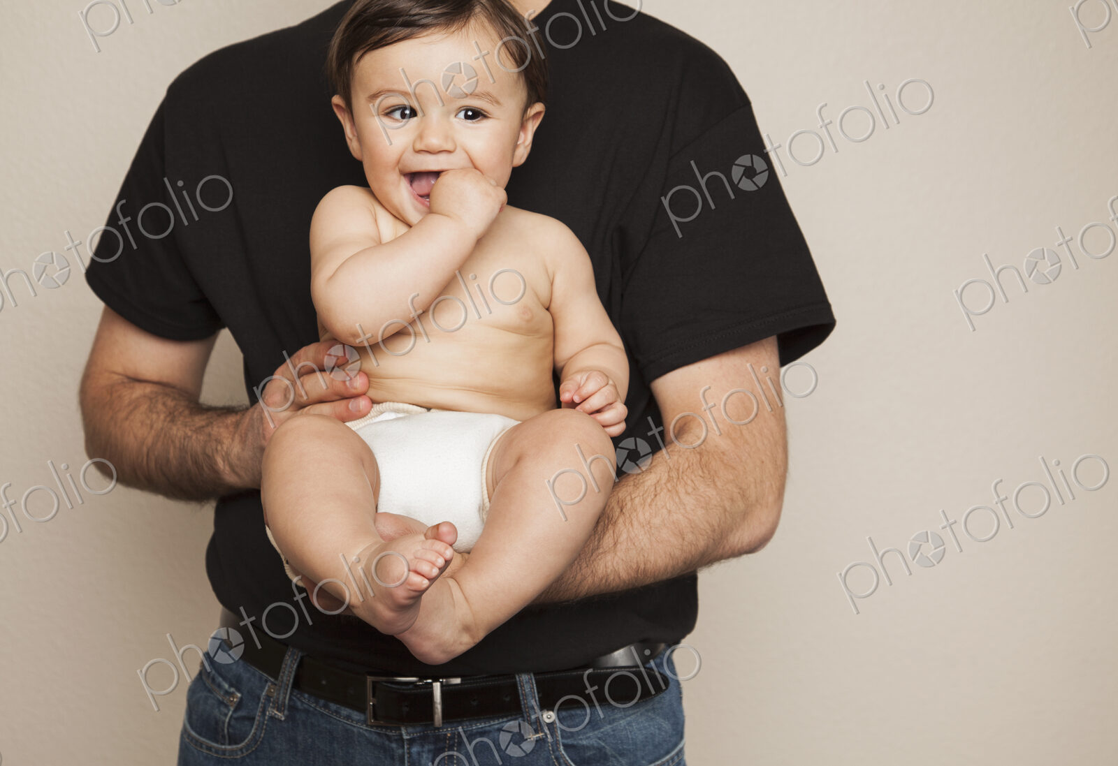 A young boy wearing cloth diapers being held by his father in his arms.