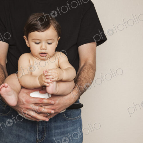 A young boy wearing cloth diapers being held by his father in his arms. A young boy wearing cloth diapers being held by his father in his arms.