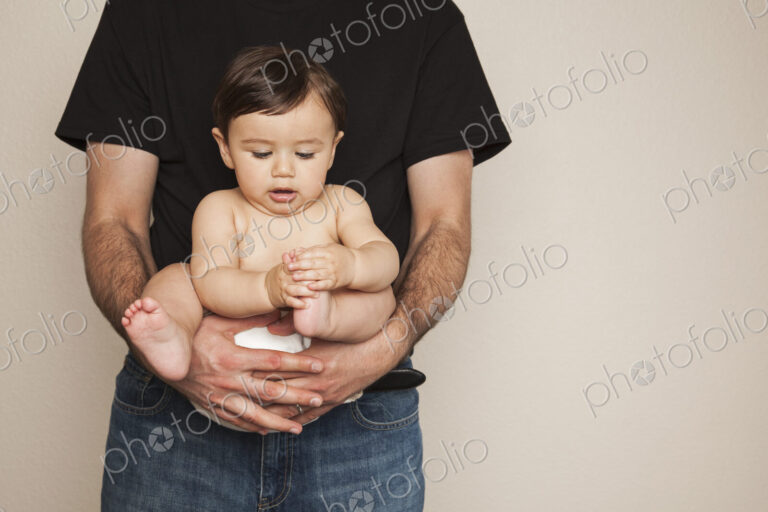 A young boy wearing cloth diapers being held by his father in his arms.
