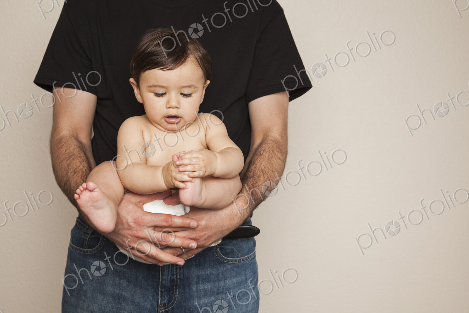 A young boy wearing cloth diapers being held by his father in his arms.