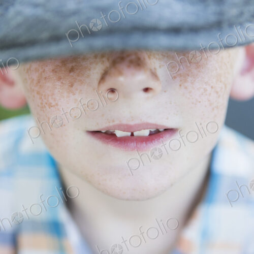 A young boy with a freckled nose, wearing a cap with a large brim.
