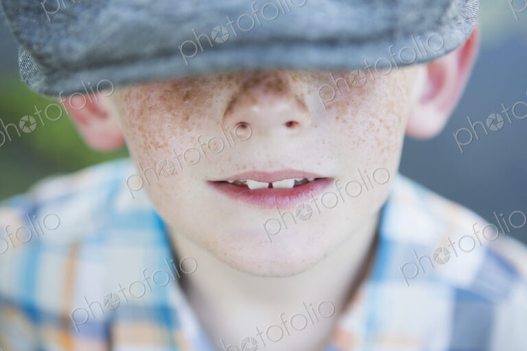 A young boy with a freckled nose, wearing a cap with a large brim.