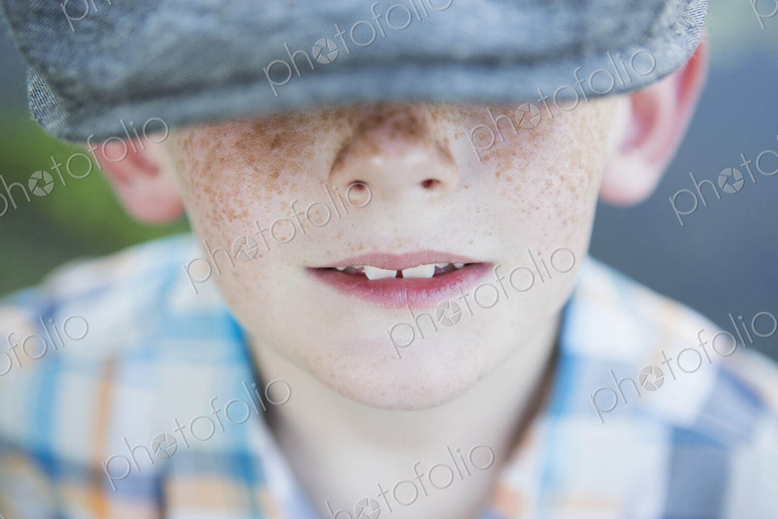A young boy with a freckled nose, wearing a cap with a large brim.