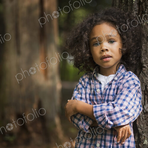 A young boy with arms folded leaning against a tree.