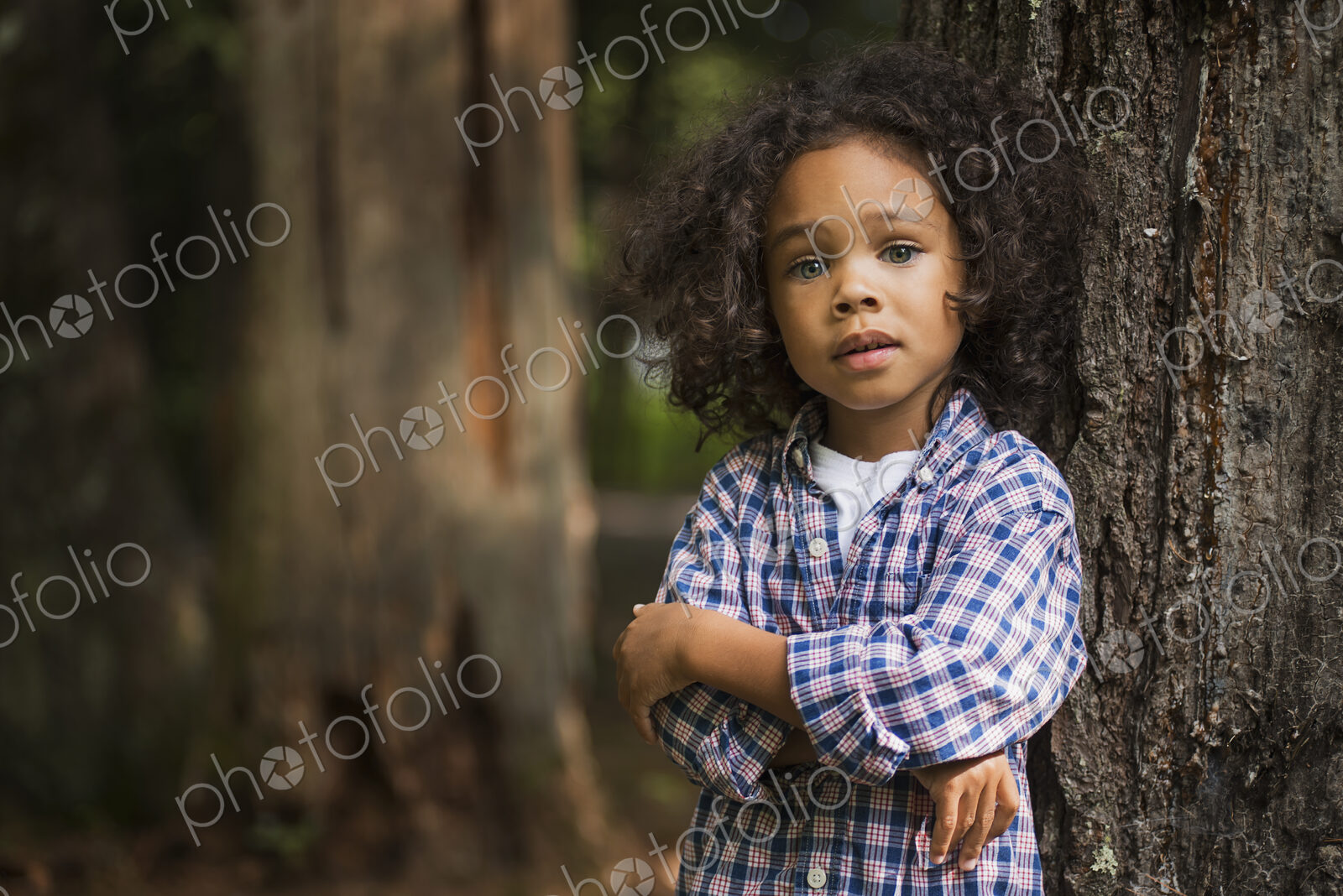 A young boy with arms folded leaning against a tree.