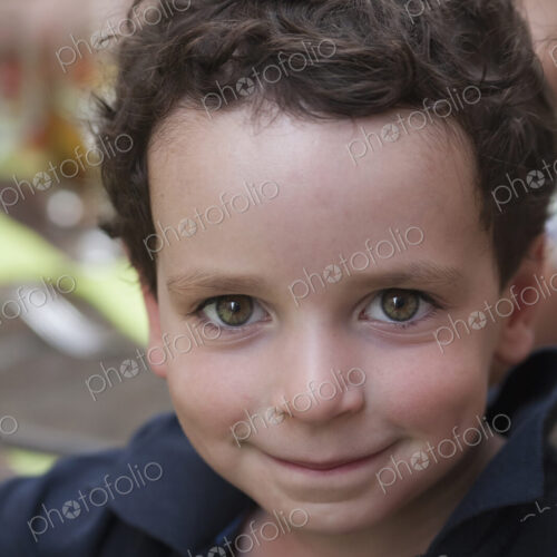 A young boy with dark hair and brown eyes, looking upwards and smiling.