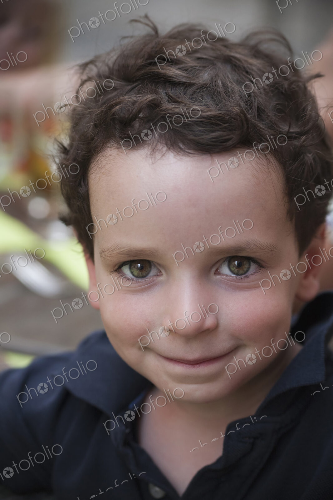 A young boy with dark hair and brown eyes, looking upwards and smiling.