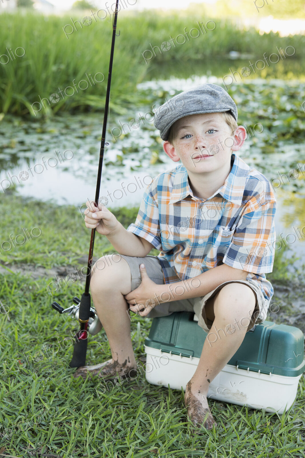 A young boy with his fishing road, by a lake or river.