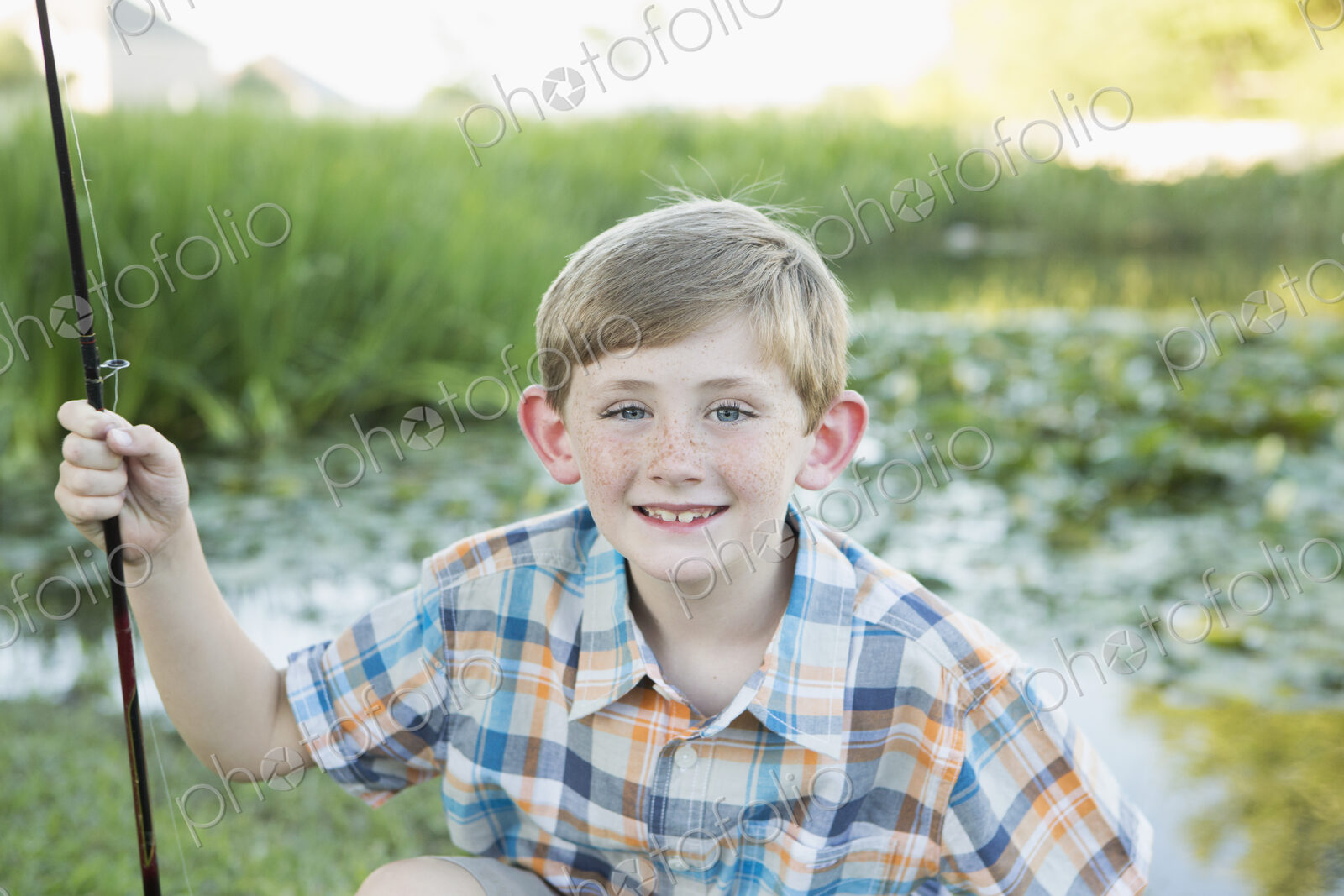 A young boy with his fishing road, by a lake or river.