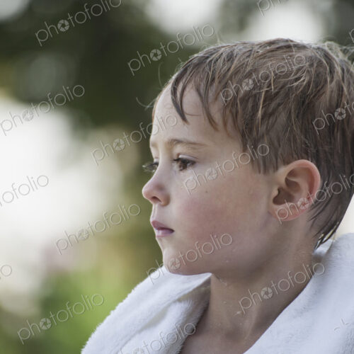 A young boy with wet hair, wrapped in a towel after swimming.