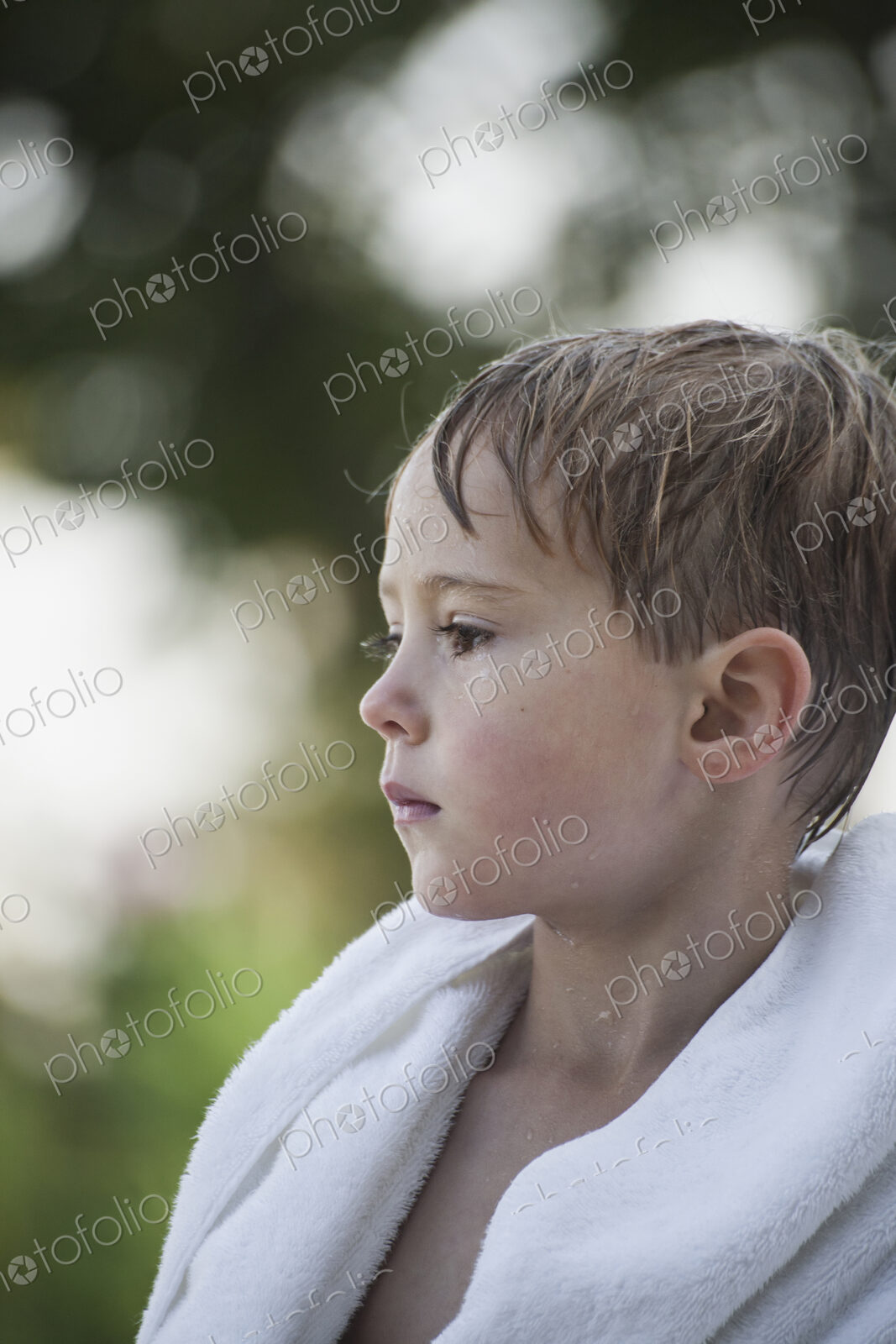 A young boy with wet hair, wrapped in a towel after swimming.