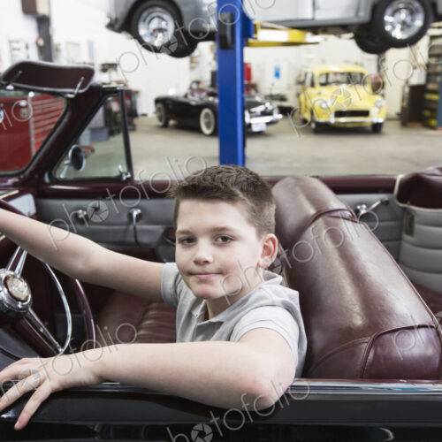 A young caucaisan boy at the wheel of an old convertible in his dad's classic car…