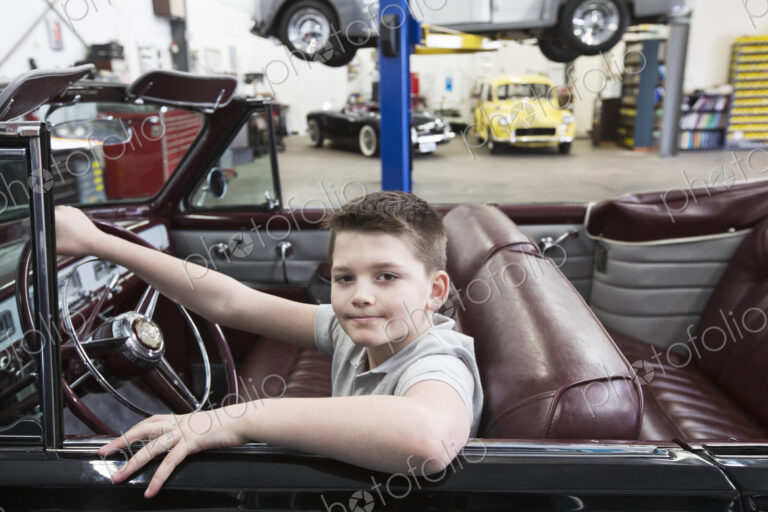 A young caucaisan boy at the wheel of an old convertible in his dad's classic car…