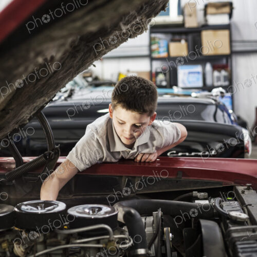 A young caucasian boy checking out an engine in his father's classic car repair shop.