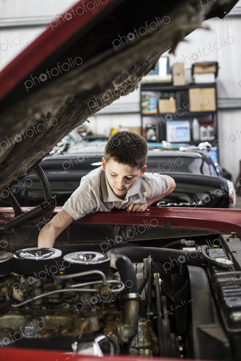 A young caucasian boy checking out an engine in his father's classic car repair shop.