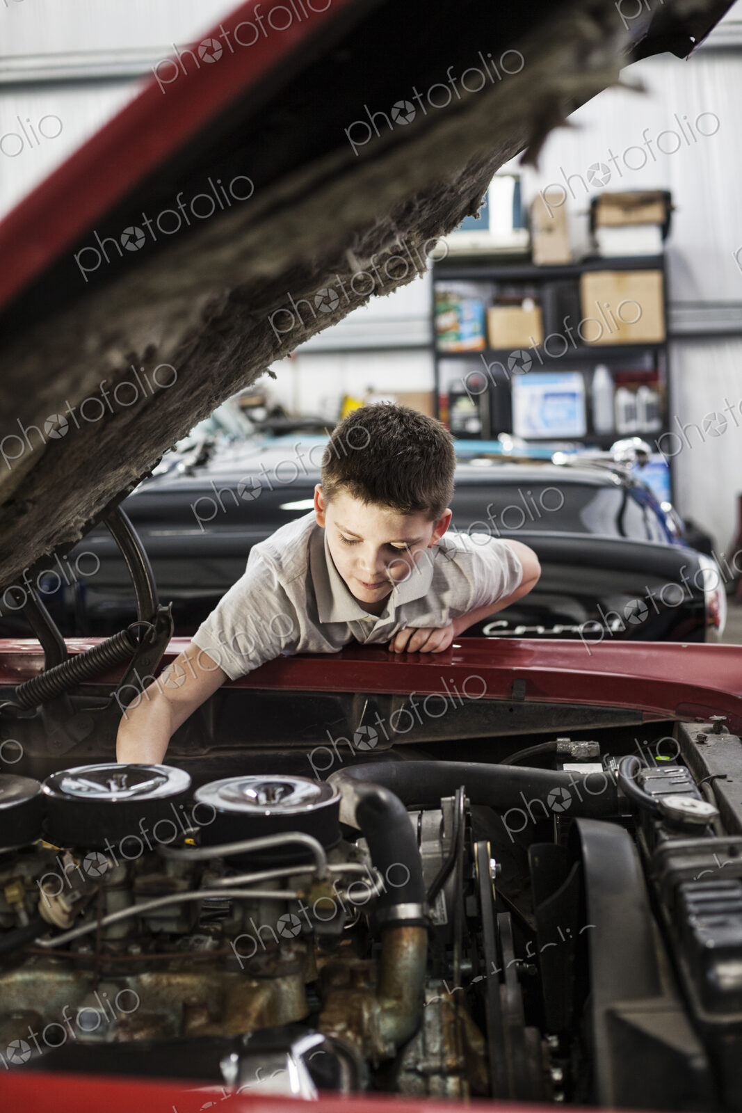 A young caucasian boy checking out an engine in his father’s classic car repair shop.