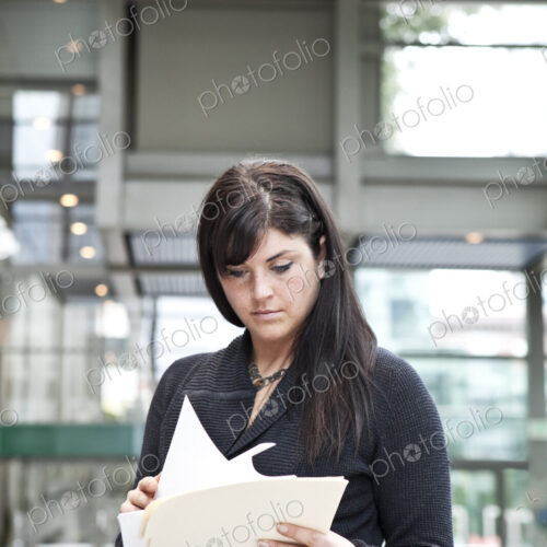 A young caucasian businesswoman going through paperwork in a convention center lobby area. A young caucasian businesswoman going through paperwork in a convention center lobby area.