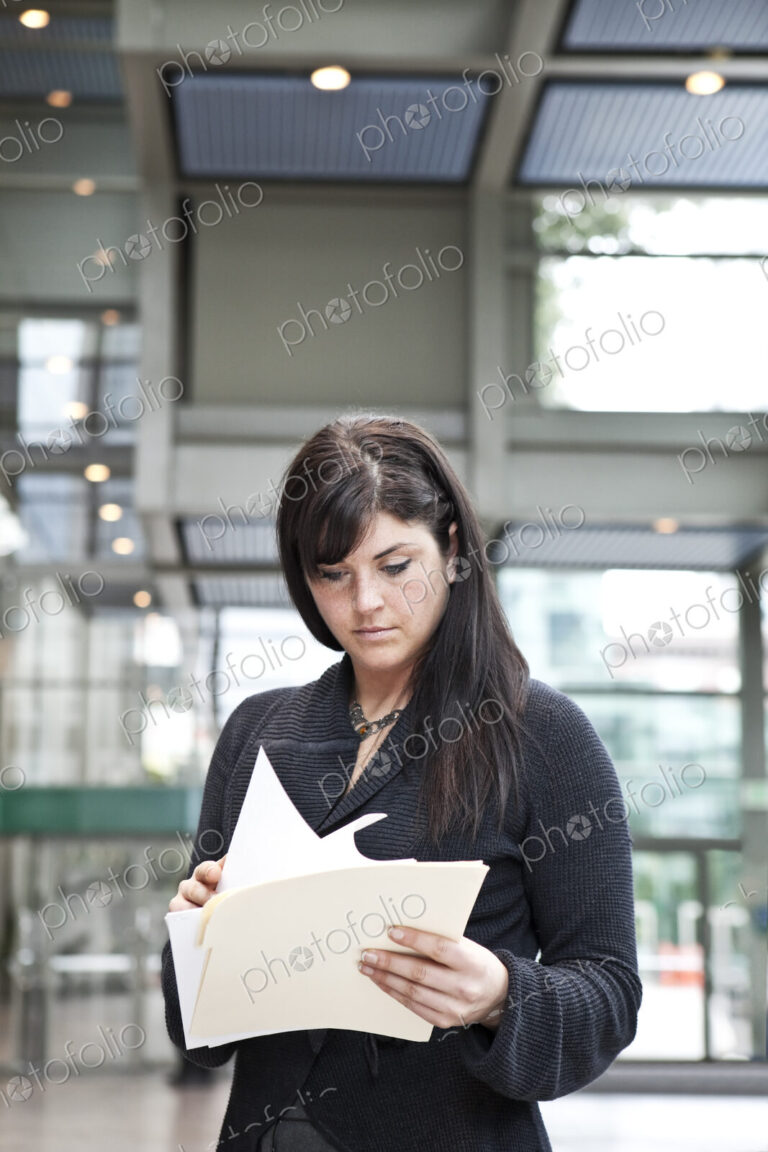 A young caucasian businesswoman going through paperwork in a convention center lobby area.