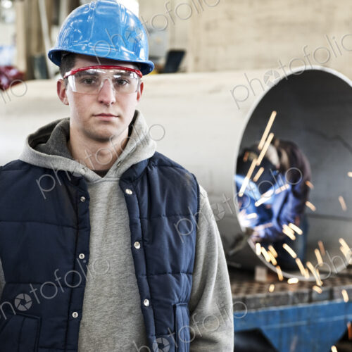A young caucasian factory worker wearing a hard hat in a sheet metal factory.