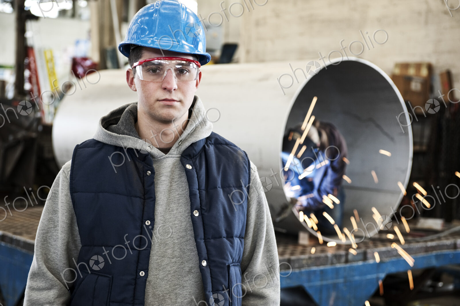 A young caucasian factory worker wearing a hard hat in a sheet metal factory.