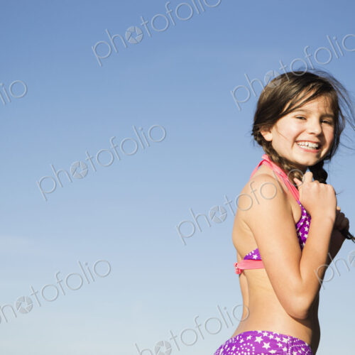 A young child in a bikini with plaited hair.