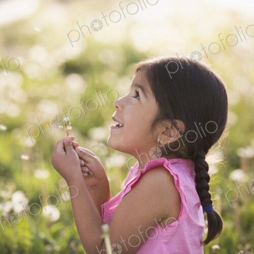 A young child in a field of flowers, blowing the fluffy seeds off a dandelion seedhead… A young child in a field of flowers, blowing the fluffy seeds off a dandelion seedhead…