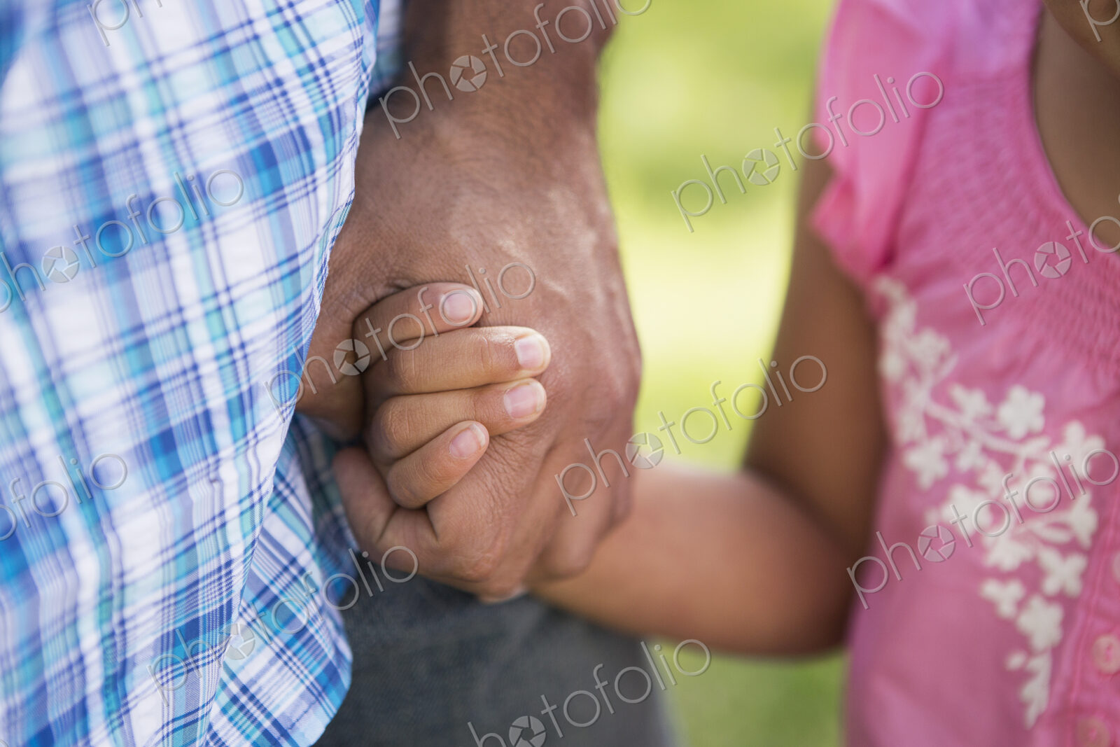 A young child in a pink dress holding her father’s hand.