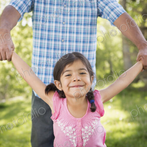 A young child in a pink dress with her arms outstretched playing with her father. A young child in a pink dress with her arms outstretched playing with her father.