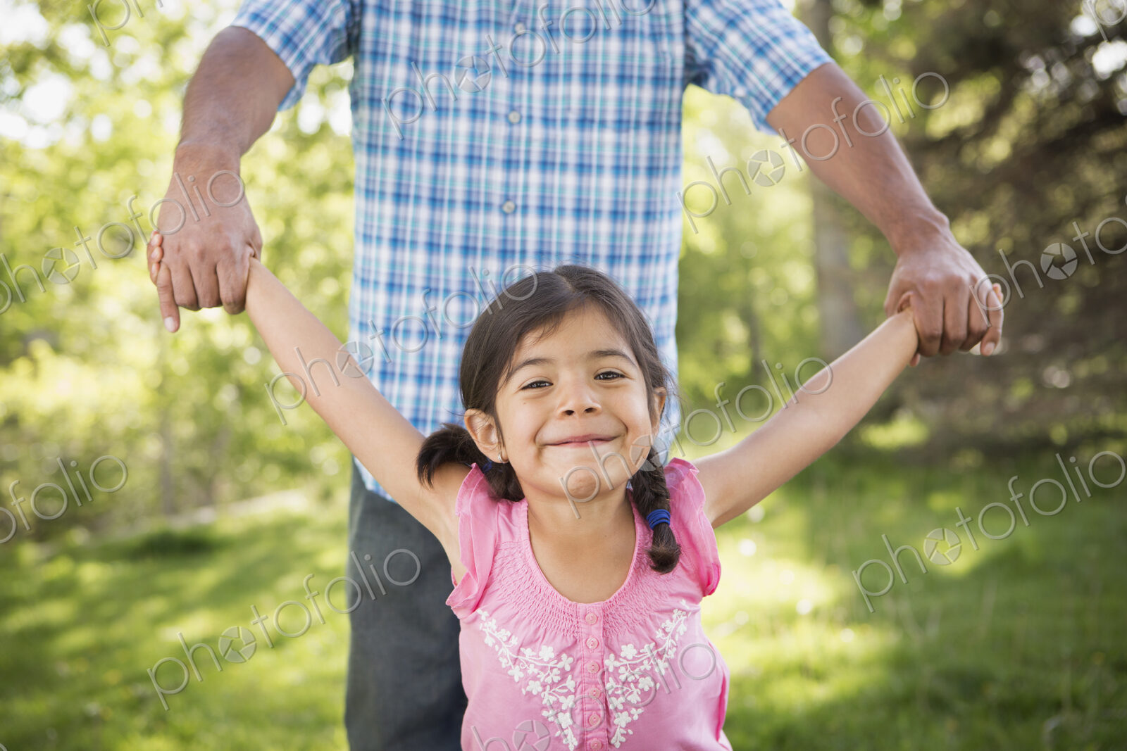 A young child in a pink dress with her arms outstretched playing with her father.