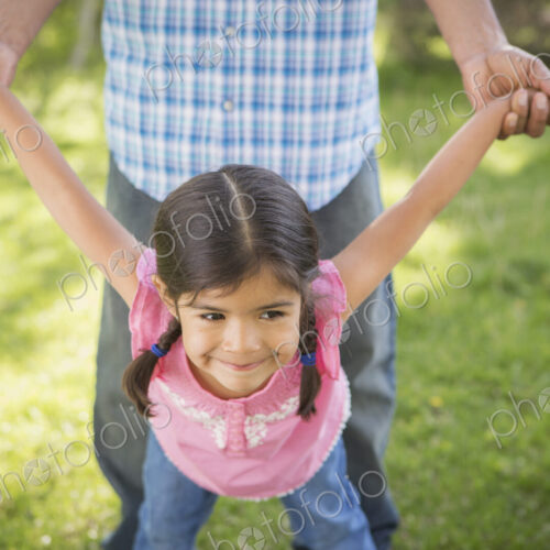 A young child in a pink dress with her arms outstretched playing with her father. A young child in a pink dress with her arms outstretched playing with her father.