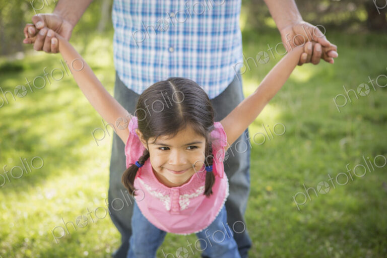 A young child in a pink dress with her arms outstretched playing with her father.