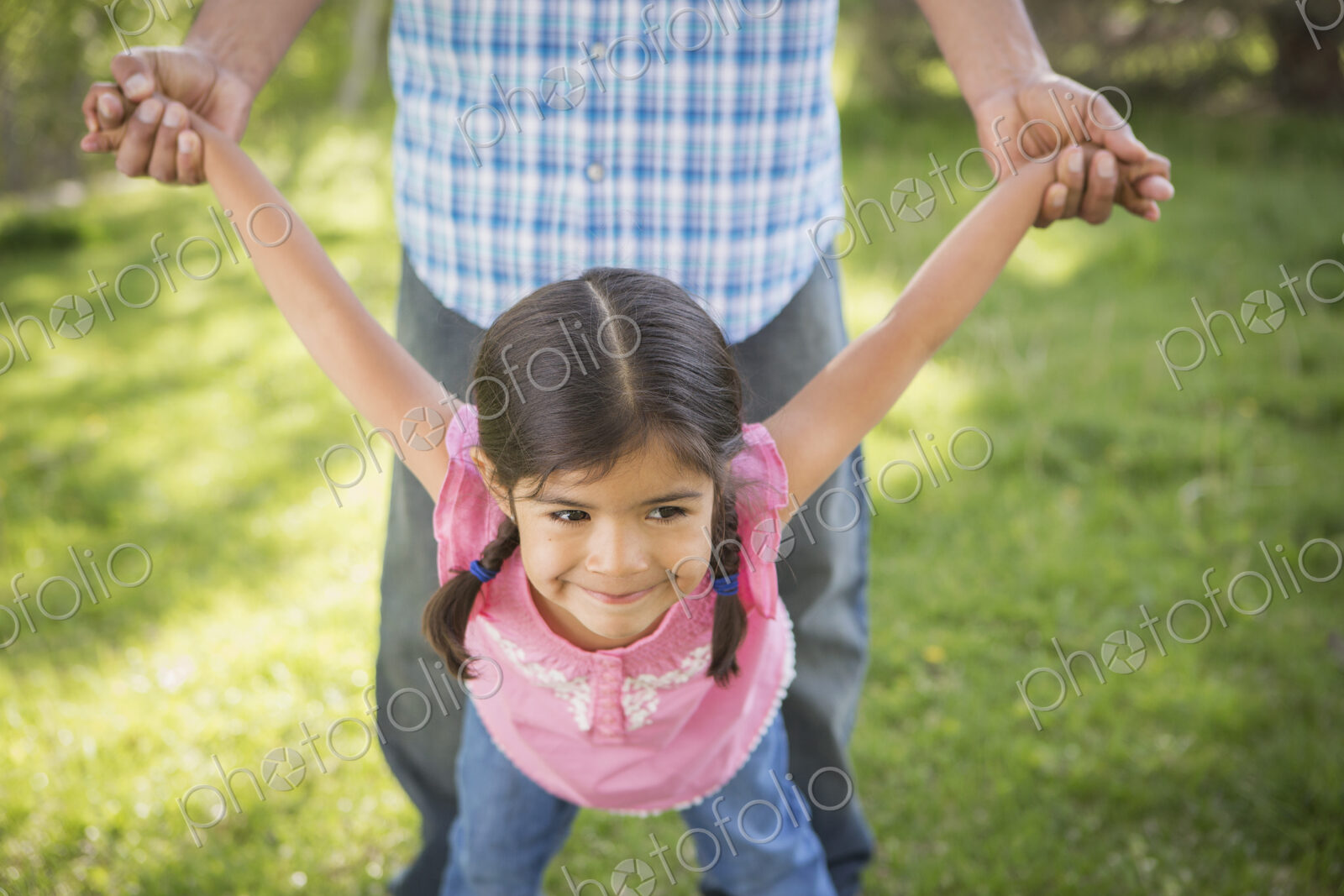 A young child in a pink dress with her arms outstretched playing with her father.