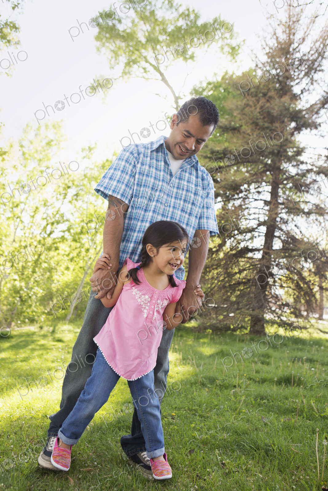 A young child in a pink dress with her feet on her father’s feet.