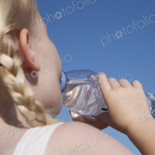 A young child with blonde hair in pigtails, drinking water from a clear bottle. A young child with blonde hair in pigtails, drinking water from a clear bottle.