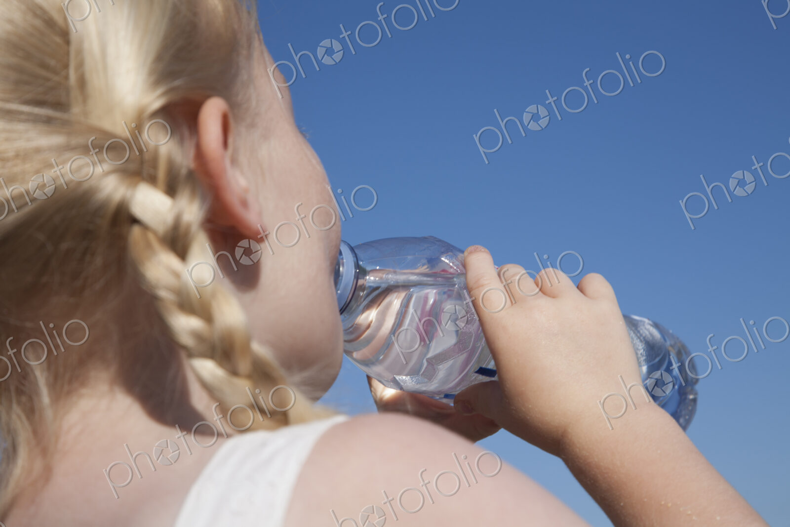 A young child with blonde hair in pigtails, drinking water from a clear bottle.