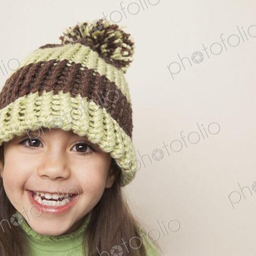 A young child with long brown hair, wearing a knitted hat with a pompom.