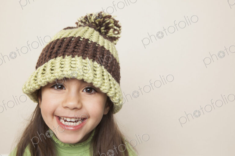 A young child with long brown hair, wearing a knitted hat with a pompom.