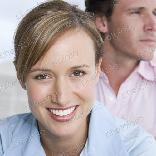 A young couple, a woman in the foreground smiling, and a man looking into the distance.