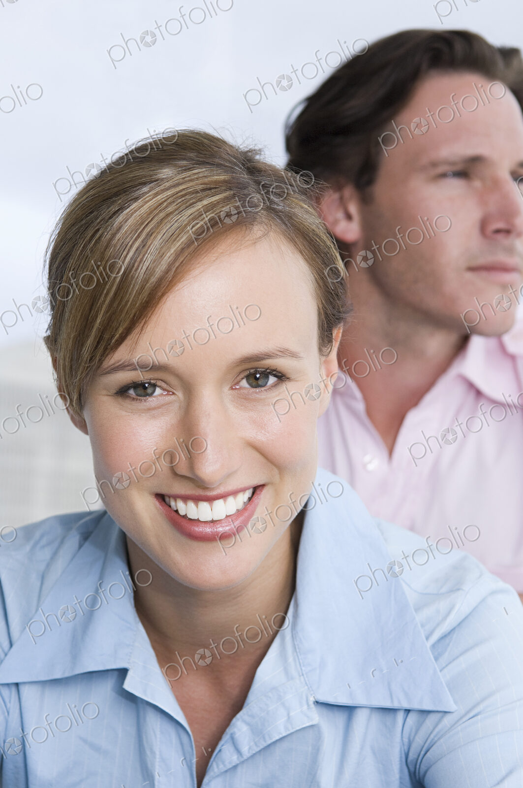 A young couple, a woman in the foreground smiling, and a man looking into the distance.