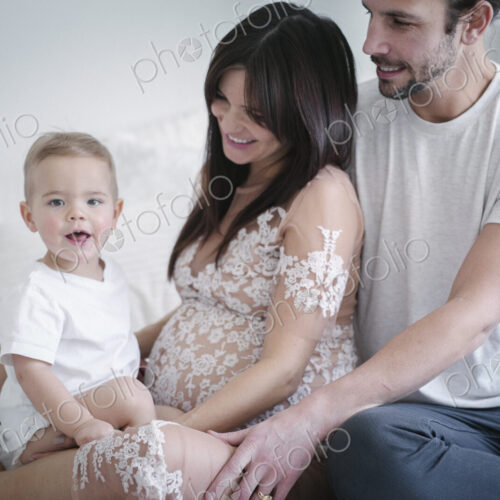 A young couple and their young son sitting together on their bed.