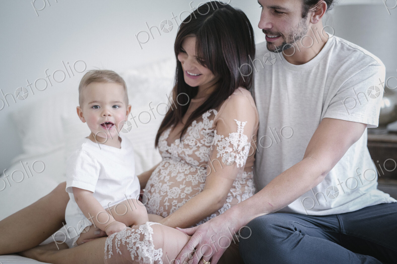 A young couple and their young son sitting together on their bed.