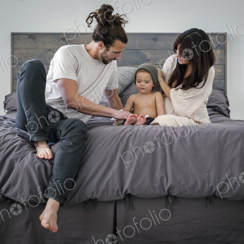 A young couple and their young son sitting together on their bed.