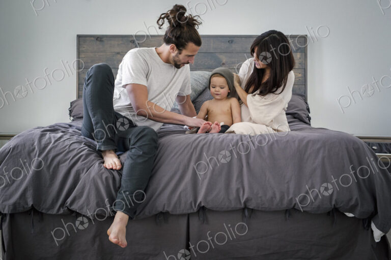 A young couple and their young son sitting together on their bed.